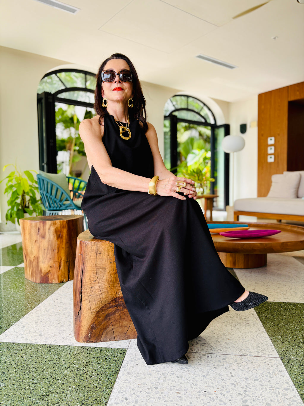 Woman seated wearing black halter maxi dress in a stylish interior setting with relaxed elegance