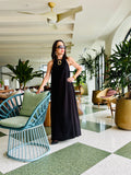 Woman wearing black halter maxi dress standing in elegant indoor setting with modern decor