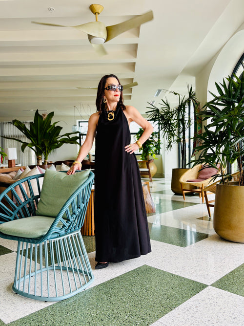 Woman wearing black halter maxi dress standing in elegant indoor setting with modern decor
