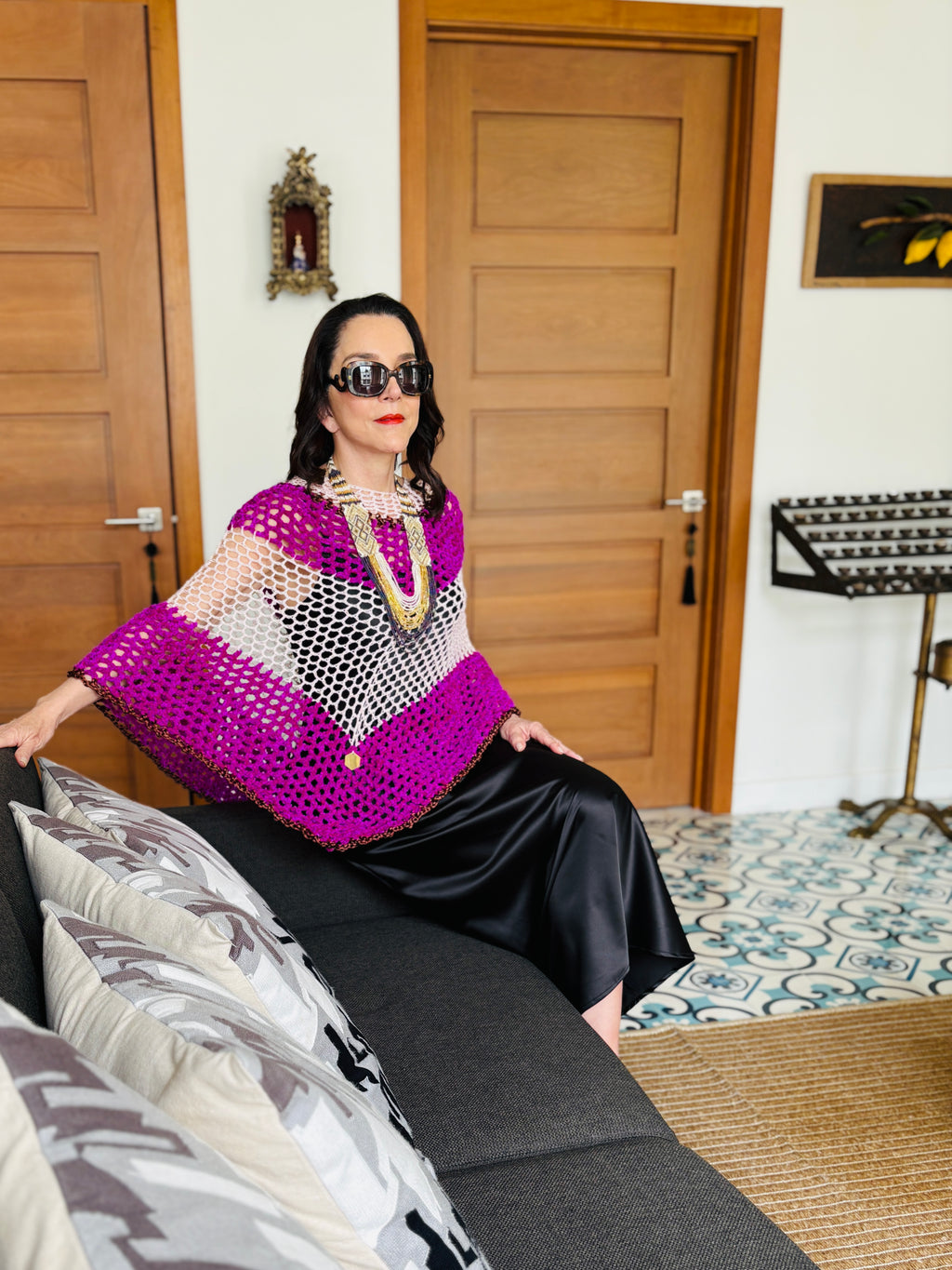 Front view of pink and white velvet poncho styled with black skirt in a sophisticated indoor setting
