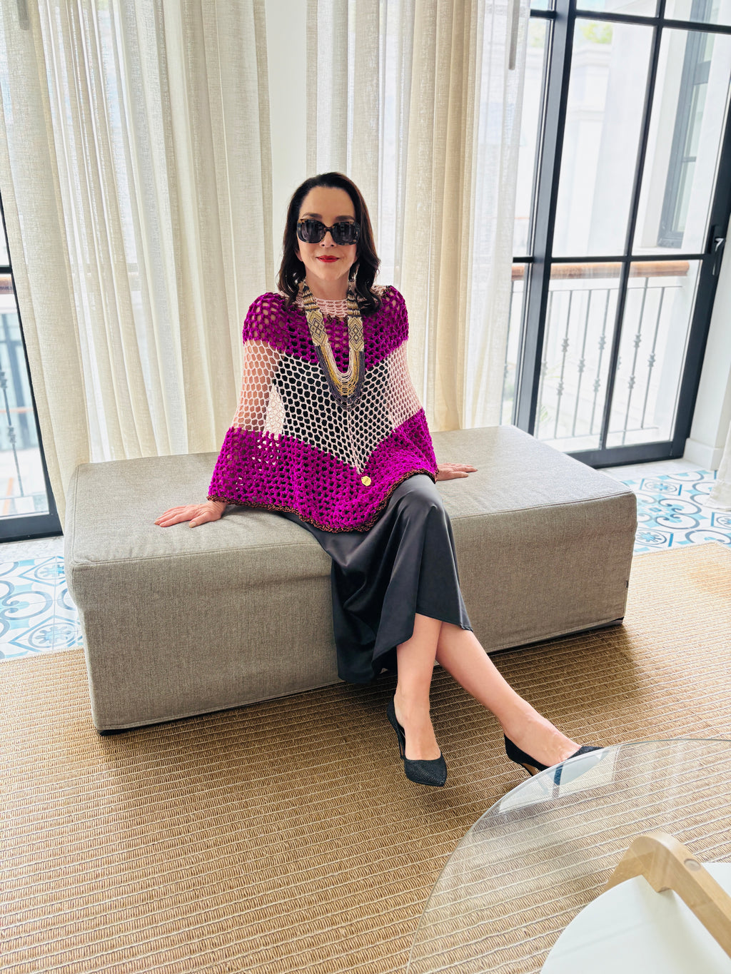 Woman wearing pink and white velvet poncho seated near window showcasing elegant drape and texture